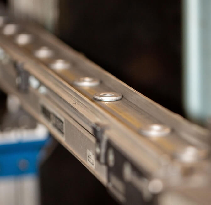 Close-up of a metal conveyor rail with several evenly spaced round rollers, part of an industrial or manufacturing setting.