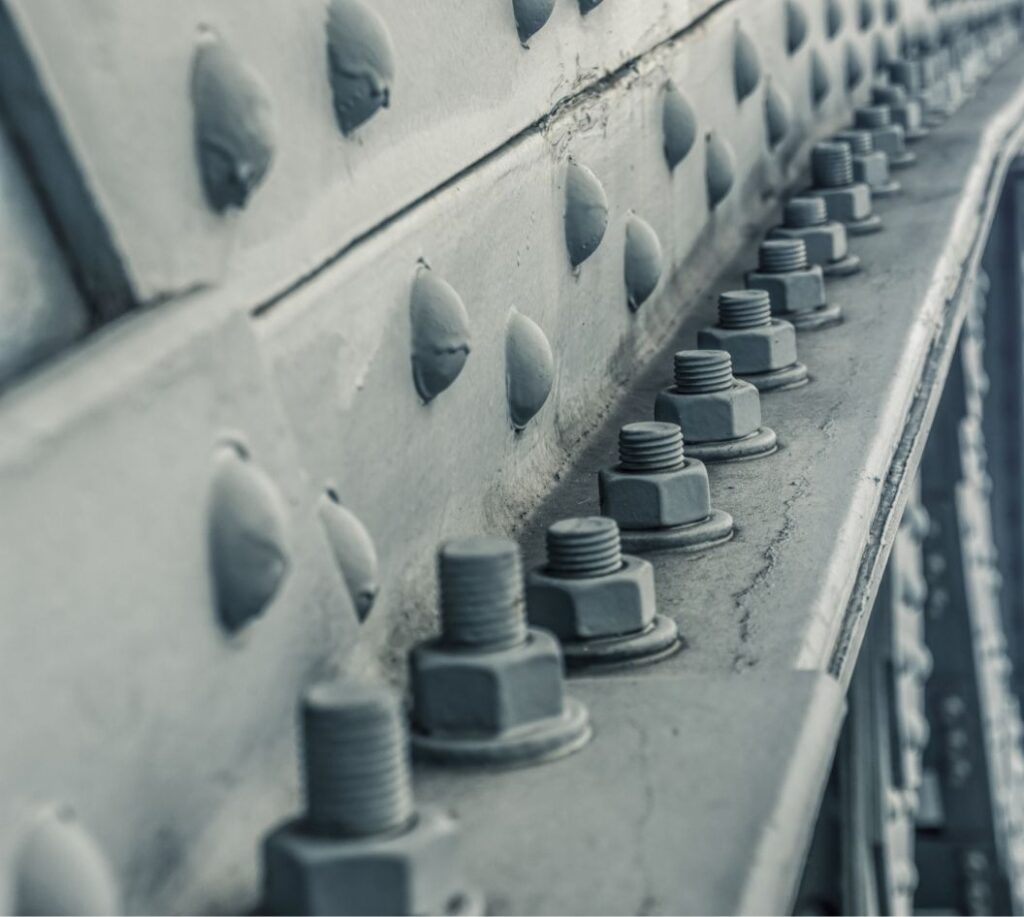 Close-up view of metal bolts and rivets on a steel beam, showing industrial construction details in a muted, gray color scheme.