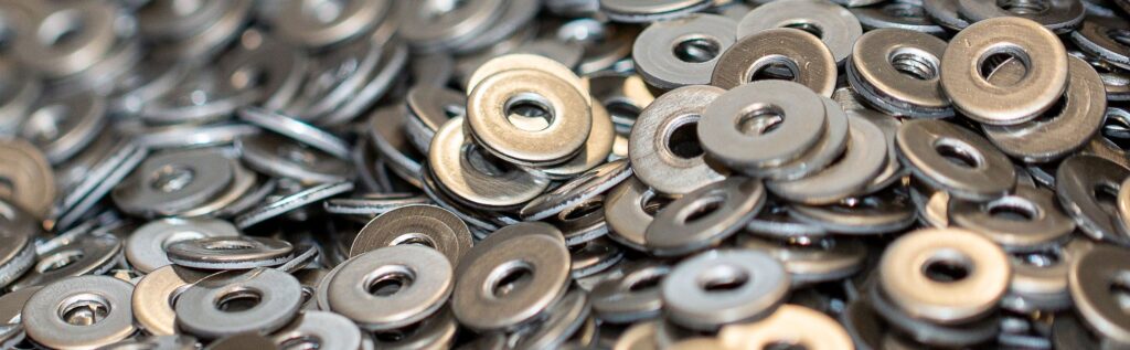 A close-up view of a large pile of metal washers, each with a central hole, showing their shiny, metallic surfaces.