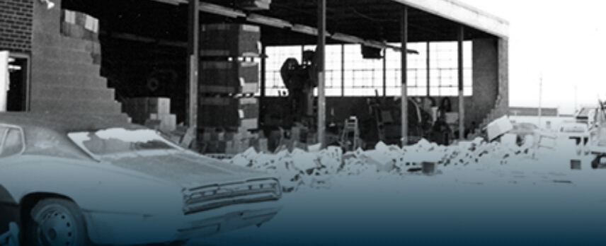 Partially destroyed warehouse with scattered debris, stacked boxes, and a damaged car parked outside.