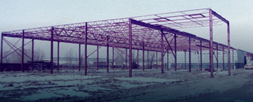 Partially constructed steel frame structure of a building on a barren, snow-dusted ground.